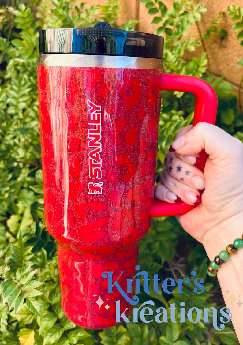 May include: Red Stanley tumbler with a leopard print design and a red handle. The tumbler has the Stanley logo in white. The text "Kritter's Kreations" is visible at the bottom of the tumbler.