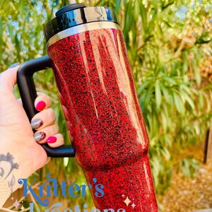 May include: A red glitter tumbler with a black handle and lid. The tumbler has a silver straw and a black rim. The text "Kitter's Kreations" is visible at the bottom of the tumbler.