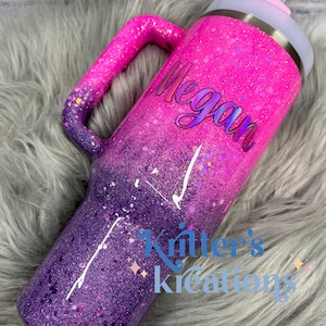 May include: A glitter-covered tumbler in shades of pink and purple, with a handle and a lid. The name "Megan" is written on the side. The words "Kritter's Kreations" are also visible. The tumbler is designed to keep drinks cold or hot.
