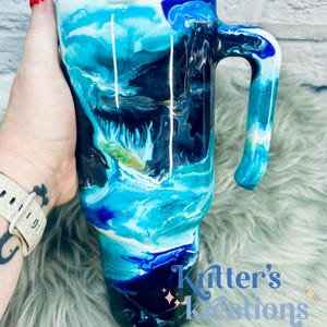 May include: A blue, black, and white abstract swirl design on a stainless steel travel mug with a handle. The mug is 20 ounces and has a double-wall insulated design to keep drinks hot or cold.