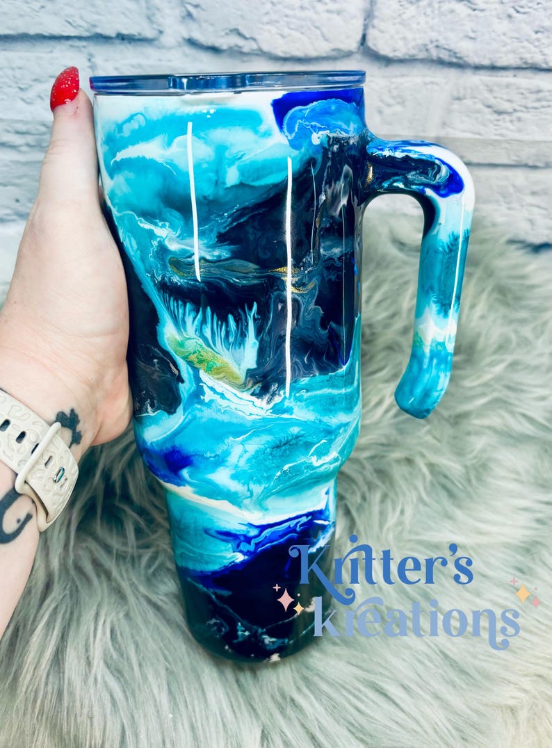 May include: A blue, black, and white abstract swirl design on a stainless steel travel mug with a handle. The mug is 20 ounces and has a double-wall insulated design to keep drinks hot or cold.