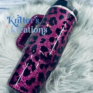 K&ouml;nnte beinhalten: Ein glitzernder, pinkfarbener Becher mit einem schwarzen Leopardenmuster. Der Becher hat einen Griff und einen schwarzen Deckel. Der Text "Kritter's Kreations" ist auf der Seite des Bechers zu sehen.