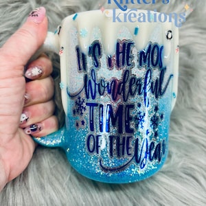 May include: A white and blue glitter mug with the text "It's the most wonderful time of the year" in blue and silver lettering.