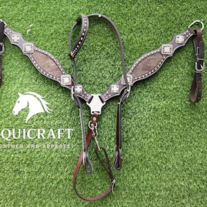 Op de afbeelding: Een bruin leren borsttuig voor paarden met zilverkleurige versieringen en een centrale decoratieve plaat. Het borsttuig heeft een gewatteerd ontwerp en staat tegen een groene achtergrond. Het logo "EQUI CRAFT LEATHER AND APPAREL" is zichtbaar.
