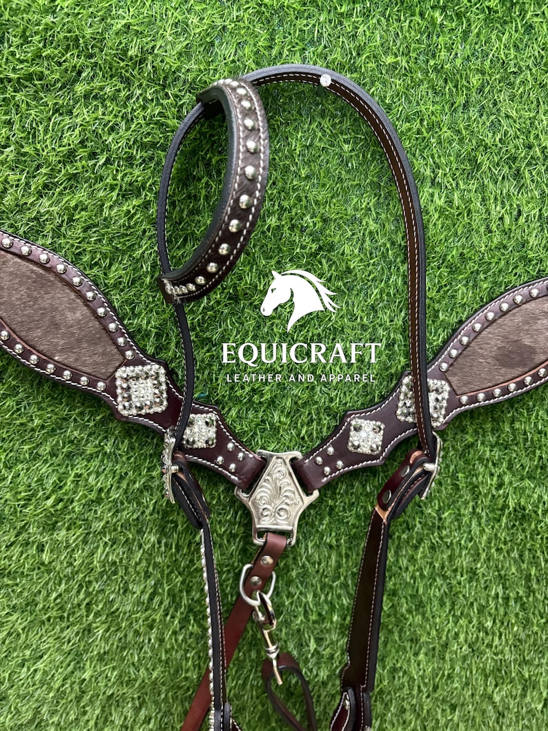Puede incluir: Una brida de caballo de cuero marr&oacute;n con tachuelas y adornos plateados. La brida presenta una cabezada marr&oacute;n oscuro, un peto con textura similar a la piel y el texto "EQUICRAFT LEATHER AND APPAREL".