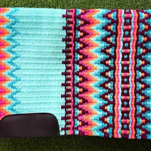 Könnte beinhalten: Türkisfarbene Pferdesattelunterlage mit einem lebendigen geometrischen Muster in Pink-, Orange-, Lila- und Blautönen. Die Unterlage hat einen dunkelbraunen Lederausschnitt für den Sattel. Für Komfort und Stil entworfen.