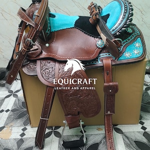 May include: A brown leather western saddle with turquoise accents and floral tooling. The saddle features a black seat, silver trim, and the text "EQUICRAFT LEATHER AND APPAREL".