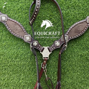 Puede incluir: Un petral de cuero marr&oacute;n para caballos con adornos plateados y una pieza decorativa central. El petral presenta un dise&ntilde;o texturizado y est&aacute; sobre un fondo verde. La marca "EQUICRAFT LEATHER AND APPAREL" es visible.
