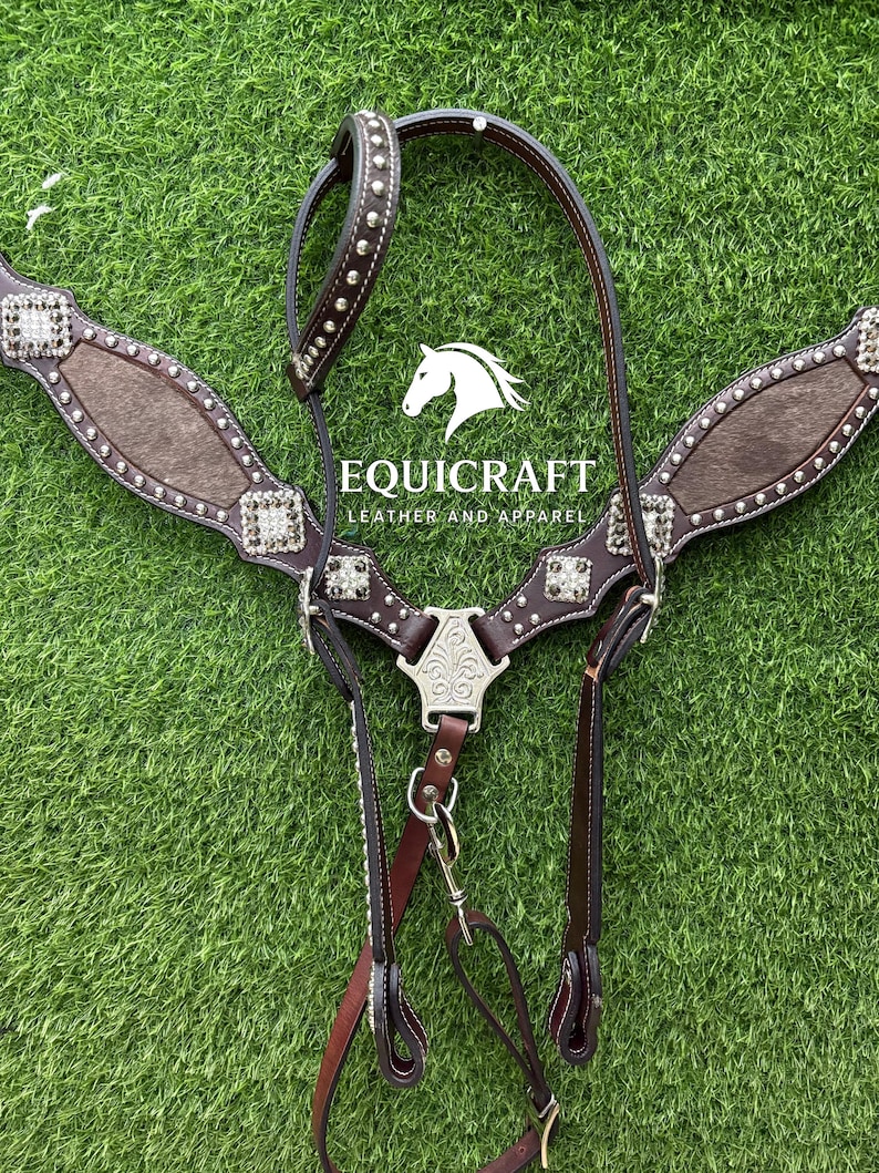 Puede incluir: Un petral de cuero marr&oacute;n para caballos con adornos plateados y una pieza decorativa central. El petral presenta un dise&ntilde;o texturizado y est&aacute; sobre un fondo verde. La marca "EQUICRAFT LEATHER AND APPAREL" es visible.