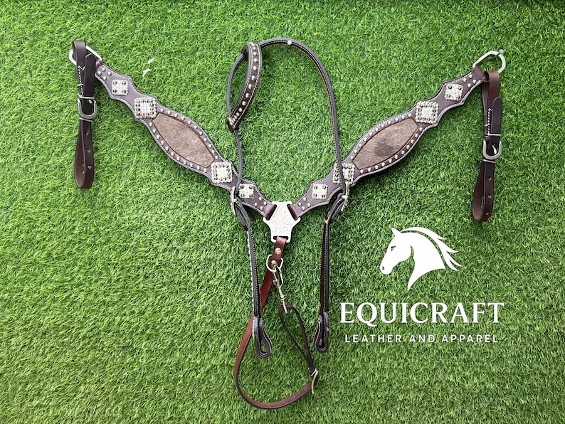 Puede incluir: Un petral de caballo de cuero marr&oacute;n con tachuelas y detalles decorativos plateados. El petral tiene una placa central y correas, con el texto "EQUICRAFT LEATHER AND APPAREL" y un logotipo de cabeza de caballo.