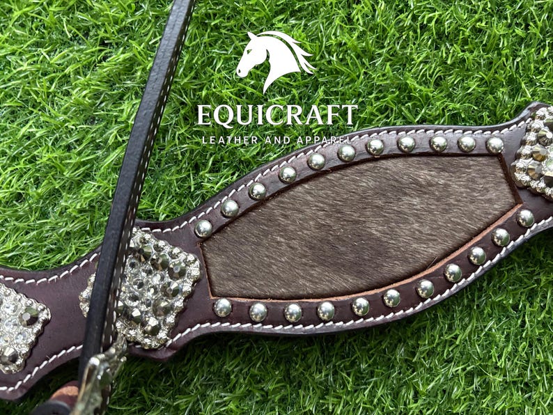 Puede incluir: Primer plano de un cabezal de caballo de cuero marr&oacute;n con tachuelas y adornos plateados. El cabezal presenta una secci&oacute;n central de piel oscura y el nombre de la marca "EQUICRAFT LEATHER AND APPAREL".