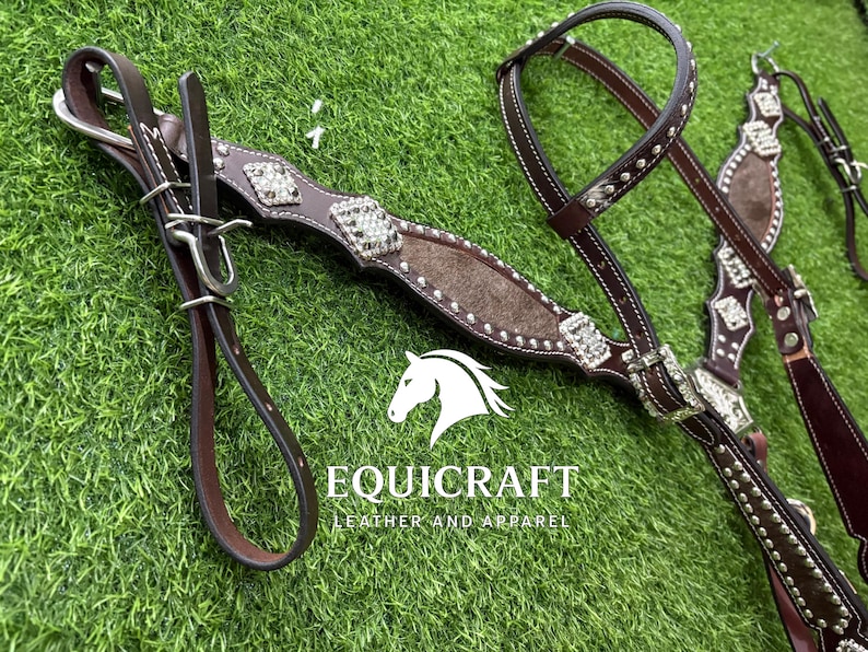 Puede incluir: Una brida de caballo de cuero marr&oacute;n con detalles plateados y pedrer&iacute;a decorativa. La brida presenta una testera y carrilleras acolchadas, con riendas a juego. La imagen tambi&eacute;n incluye el texto "EQUICRAFT LEATHER AND APPAREL".