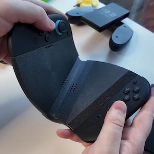 Puede incluir: Mando de juegos negro con un joystick azul y un agarre texturizado. El mando tiene botones etiquetados A, B, X e Y. El mando se sostiene con dos manos.