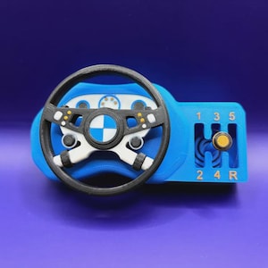 May include: A blue and black toy steering wheel with a gear shift. The steering wheel has a black rim and white accents. The gear shift has the numbers 1, 2, 3, 4, 5, and R. The center of the steering wheel has a logo.