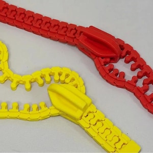 Op de afbeelding: Twee plastic ritsspeelgoed, één rode en één gele, worden getoond tegen een lichtgrijze achtergrond. De rode rits is volledig gesloten, terwijl de gele gedeeltelijk open is.