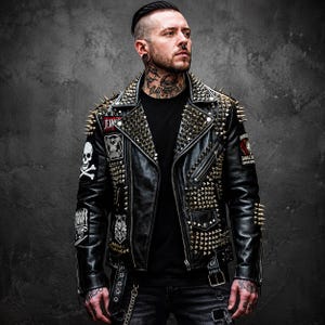 May include: A black leather motorcycle jacket featuring silver-toned metal spikes on the shoulders and lapels, multiple silver zippers, and various patches including a skull and crossbones design on the right sleeve and text on the left sleeve.
