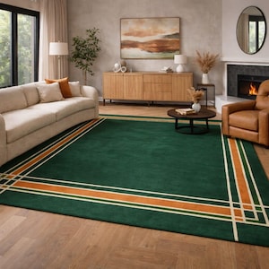 May include: A large, rectangular green rug with a geometric border design. The border features a combination of orange, white, and green stripes. The rug is placed in a living room setting with a sofa, fireplace, and wooden furniture.