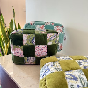 May include: Three square, quilted cushions in shades of green and floral patterns. The cushions are arranged on a light-coloured surface. The patchwork design features squares of solid green velvet and patterned fabric.
