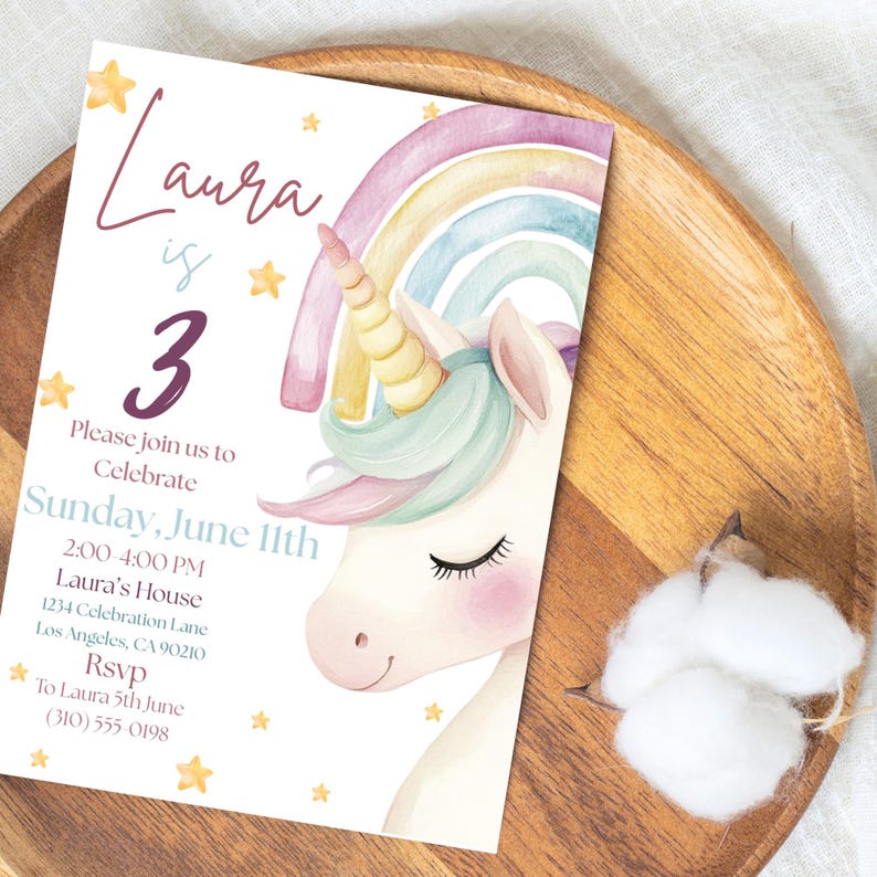 May include: A birthday invitation with a watercolour unicorn, rainbow, and stars. The invitation says "Laura is 3" and includes event details: Sunday, June 11th, 2:00-4:00 PM, and an RSVP. The invitation is on a wooden tray.