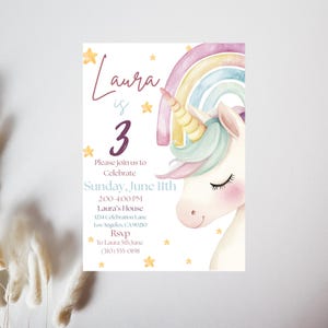 May include: A pastel-coloured invitation card with a unicorn illustration and a rainbow. The text reads "Laura is 3" with event details: Sunday, June 11th, 2:00-4:00 PM, and an RSVP. The design includes stars and a soft, watercolour style.