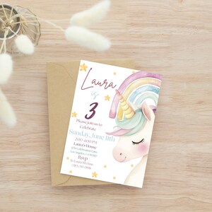 May include: A birthday invitation featuring a watercolour unicorn with a rainbow and stars. The invitation reads "Laura is 3" with event details. The invitation is on a white background with a brown envelope.