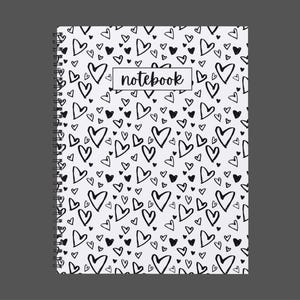 May include: A spiral-bound notebook with a white cover covered in a pattern of black hearts of varying sizes. The word "notebook" is in a rectangular box on the cover. The background is a solid gray.