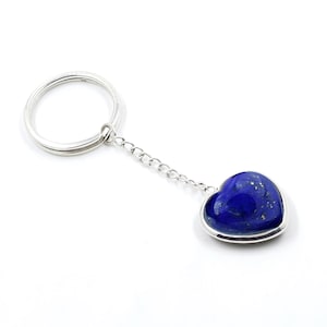 May include: A silver keychain with a heart-shaped pendant. The pendant is a deep blue stone with gold flecks, set in a silver bezel. The keychain has a silver ring and a chain.
