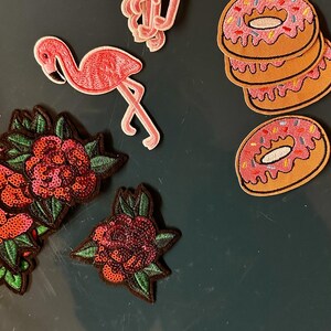 Può includere: Toppe ricamate raffiguranti fenicotteri rosa, ciambelle con glassa rosa e zuccherini, e rose rosse con foglie verdi. Ideali per decorare abbigliamento o accessori.