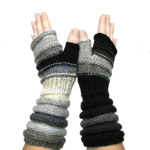 May include: A pair of fingerless gloves with a striped pattern in shades of gray, black, and white. The gloves are knit and have a long cuff.