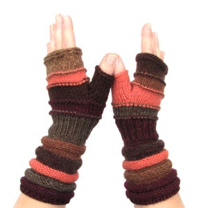May include: A pair of fingerless gloves with a striped pattern in shades of brown, orange, and burgundy. The gloves are made of knitted fabric and have a warm, cozy look.