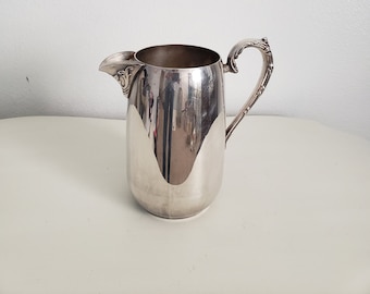 May include: A silver pitcher with a decorative handle and spout. The pitcher is polished and shiny.