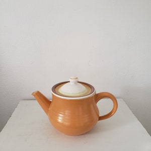 May include: A brown ceramic teapot with a white lid and a brown handle. The teapot has a striped design around the lid.