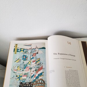 May include: A colorful illustration of a ship with many flags from different countries. The ship is sailing on a body of water with a mountain range in the background. The text "The Expansion of Europe" is printed in black on a white background.