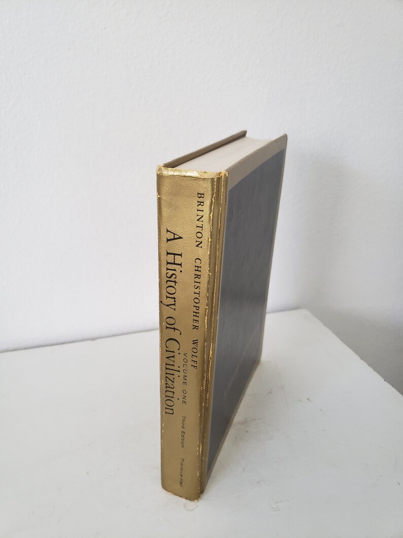 May include: A gold-colored book titled "A History of Civilization" by Christopher Wolff. The book is a third edition and volume one.