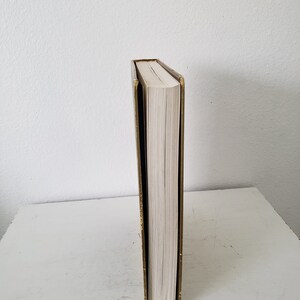 May include: A gold-colored book with a white spine and a black cover. The book is standing upright on a white surface.