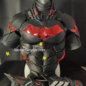 Pode incluir: Conjunto de armadura cosplay preto e vermelho com textura de fibra de carbono. A peça do peito apresenta um símbolo de morcego vermelho. O conjunto inclui uma peça de peito, ombreiras e protetores de antebraço. O texto "SapnahCosplayStore" é visível.