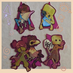 Puede incluir: Conjunto de cuatro pegatinas de personajes. Cada pegatina presenta un diseño de personaje diferente con una pose y una combinación de colores únicas. Las pegatinas están cortadas en forma de triángulo morado. Una pegatina tiene el texto "HEY!!".