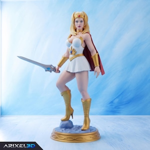 Può includere: Una action figure bionda in piedi su una base circolare, che indossa un abito bianco con un emblema dorato, guanti dorati e stivali dorati. Un mantello rosso pende dalle spalle e una spada argentata con una gemma blu è tenuta nella mano destra.