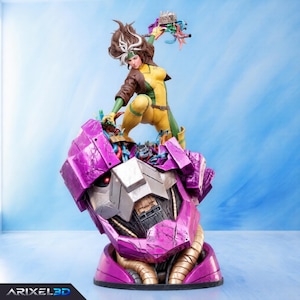 May include: A detailed figurine of a character with brown hair and a white streak, wearing a yellow and green bodysuit with a brown jacket, standing atop a large, damaged purple robotic head with a glowing red eye and exposed mechanical wiring.
