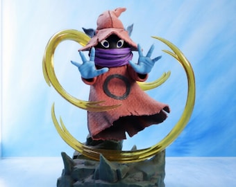 May include: A figurine of a hooded character with a dark face, large white eyes, and a purple neck wrap. The figure wears a textured red robe with a black circle emblem, has blue hands raised, and is surrounded by a translucent gold energy ring.