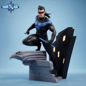 May include: A Nightwing figurine featuring a black suit with a blue chest emblem, black mask, and two blue escrima sticks. The character stands on a gray stone gargoyle and brick base next to a black building structure with illuminated yellow windows.
