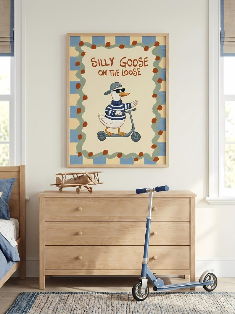 a wooden dresser with a framed poster of a cartoon goose riding a scooter on the wall above it. The poster has a playful and whimsical design, with the goose wearing sunglasses and a striped sweater. The dresser also has a small model airplane on top.