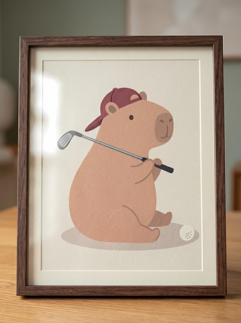 May include: A framed print showing a cartoon capybara wearing a maroon baseball cap and holding a golf club. A golf ball is on the ground. The capybara is light brown, and the frame is dark brown.