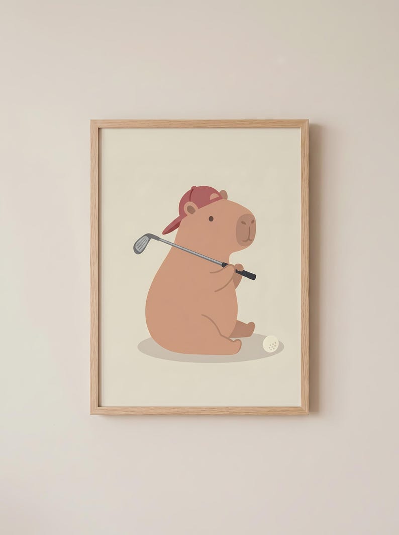 May include: A framed print of a cartoon capybara wearing a red baseball cap and holding a golf club. A white golf ball is on the ground. The capybara is light brown, and the background is a soft beige.