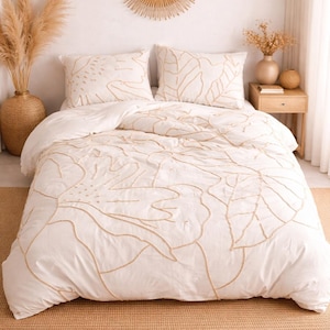 Könnte beinhalten: Weißer Bettbezug und zwei Kissenbezüge mit beigem Blattmuster. Die Bettwäsche liegt auf einem Bett mit einem gewebten Teppich. Über dem Bett hängt ein runder Spiegel mit Sonnenstrahlenrahmen.