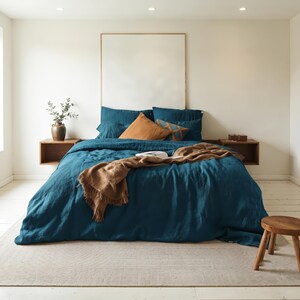 May include: A deep teal linen duvet cover set on a bed with matching pillowcases, accented by a solid rust-colored throw pillow, a patterned rust-colored accent pillow, and a textured brown throw blanket draped across the foot of the bed.