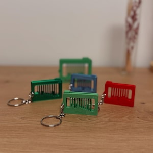 Könnte beinhalten: Eine Sammlung farbenfroher Schlüsselanhänger in Grün, Blau und Rot. Jeder Schlüsselanhänger hat ein rechteckiges Design mit vertikalen Stäben und einem silbernen Schlüsselring. Die Schlüsselanhänger liegen auf einer Holzoberfläche.