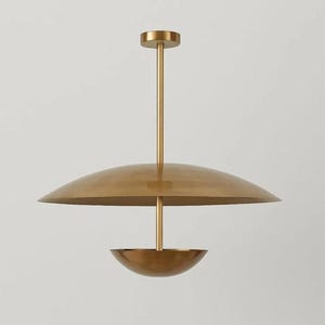 May include: A brass-colored, modern pendant light fixture. The light has a large, curved shade and a smaller, bowl-shaped element below. The fixture is suspended from a single rod attached to a circular ceiling mount. The overall design is minimalist and elegant.