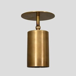 Può includere: Una lampada a sospensione cilindrica color ottone, con una parte superiore circolare e un corpo cilindrico. La luce ha un design moderno ed è sospesa al soffitto. L'apparecchio è in metallo e ha una finitura metallica calda.