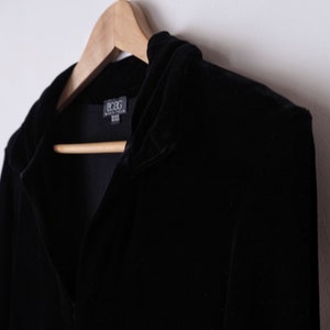 K&ouml;nnte beinhalten: Eine schwarze Samtjacke mit Kapuze und einem BCBG Max Azria-Etikett.